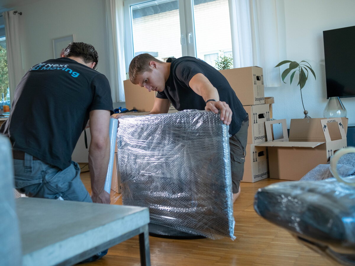 Jannes Wesselmann und ein Helfer schützen ein Möbelstück mit Luftpolsterfolie